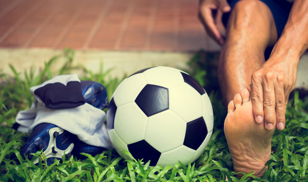 Persona che esegue un esercizio a piedi scalzi accanto a un pallone da calcio, enfatizzando l'importanza dell'allenamento plantare per migliorare la performance sportiva.