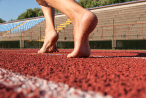 Persona con piedi scalzi che corre su una pista, illustrando il movimento naturale del barefoot running.